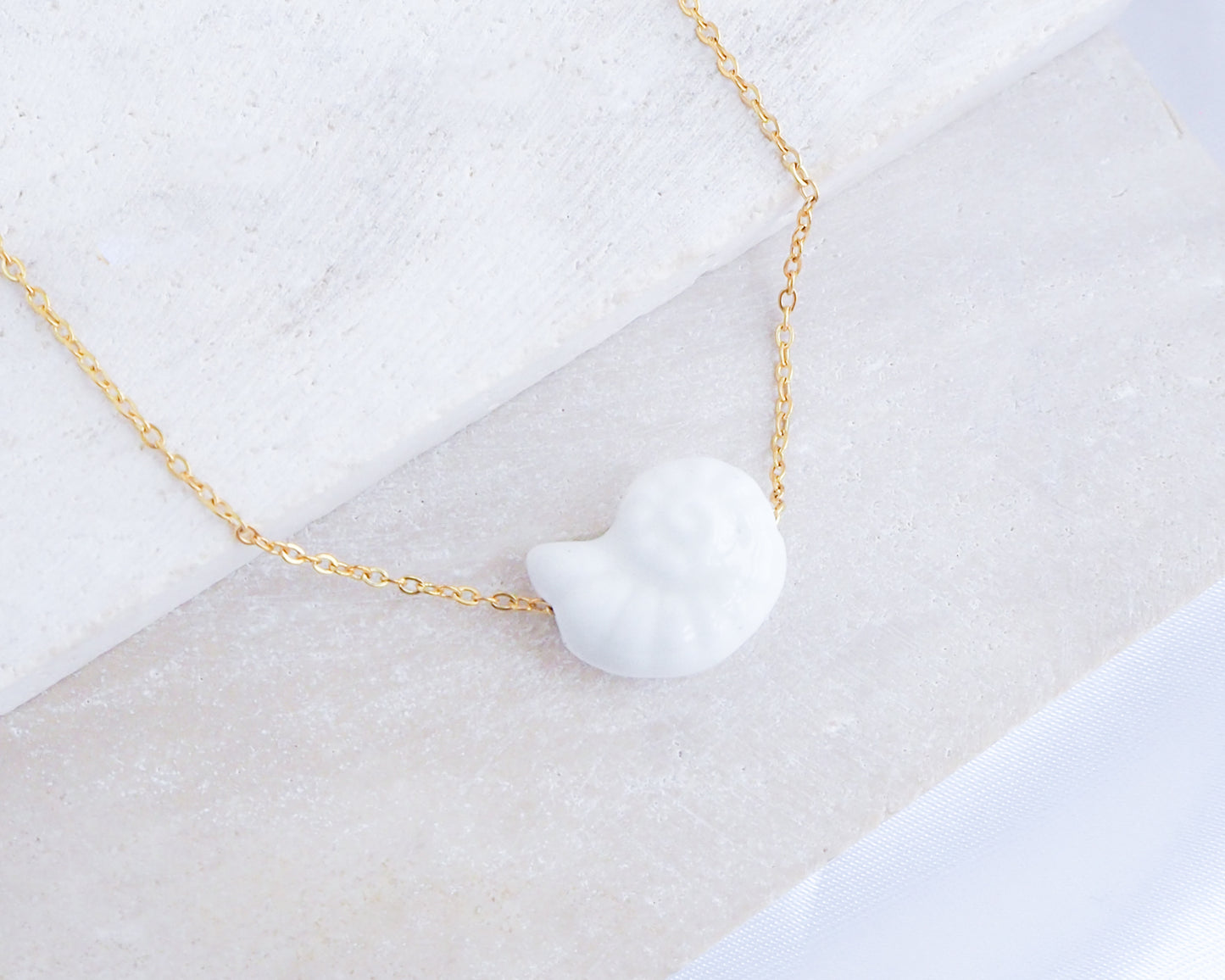 White Ceramic Seashell Nautilus Gold Necklace displayed on stone
