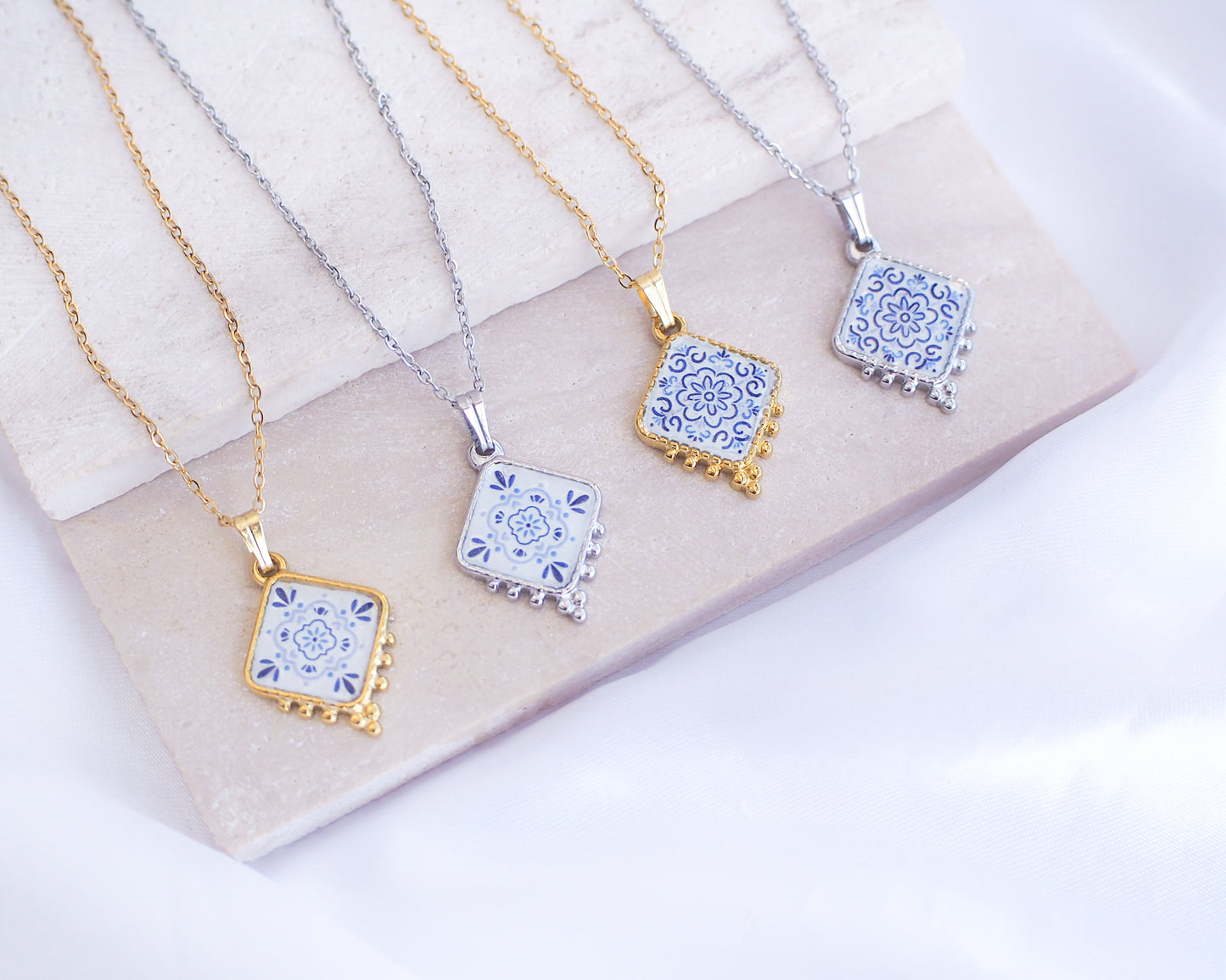 Close up of Portuguese Tile Necklace Floral Blue Gold and Silver on stone displayed. Made with 18k gold stainless steel or silver stainless steel and white blue floral pendant inspired by the Portuguese Azulejo design pattern. 