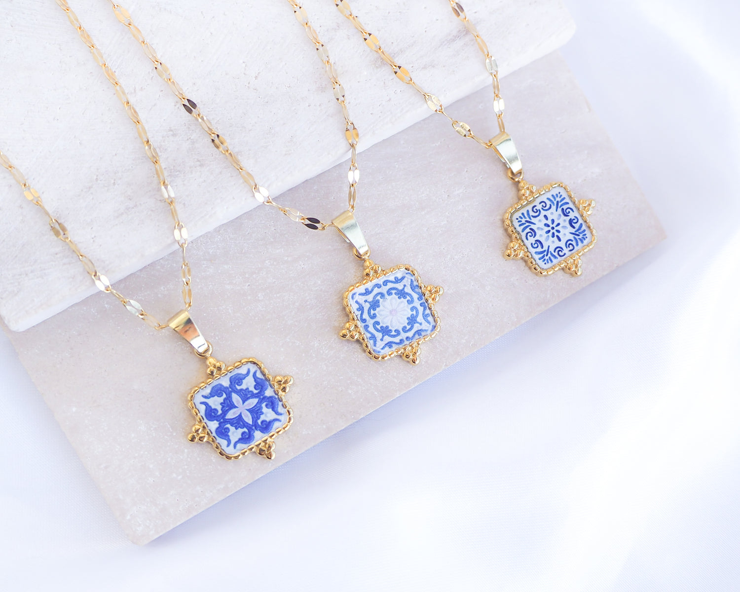 Close up of Gold Portuguese Tile Square Necklaces Blue on stone displayed. Made with 18k gold stainless steel or silver stainless steel and white blue mosaic pendant inspired by the Portuguese Azulejo design pattern. 