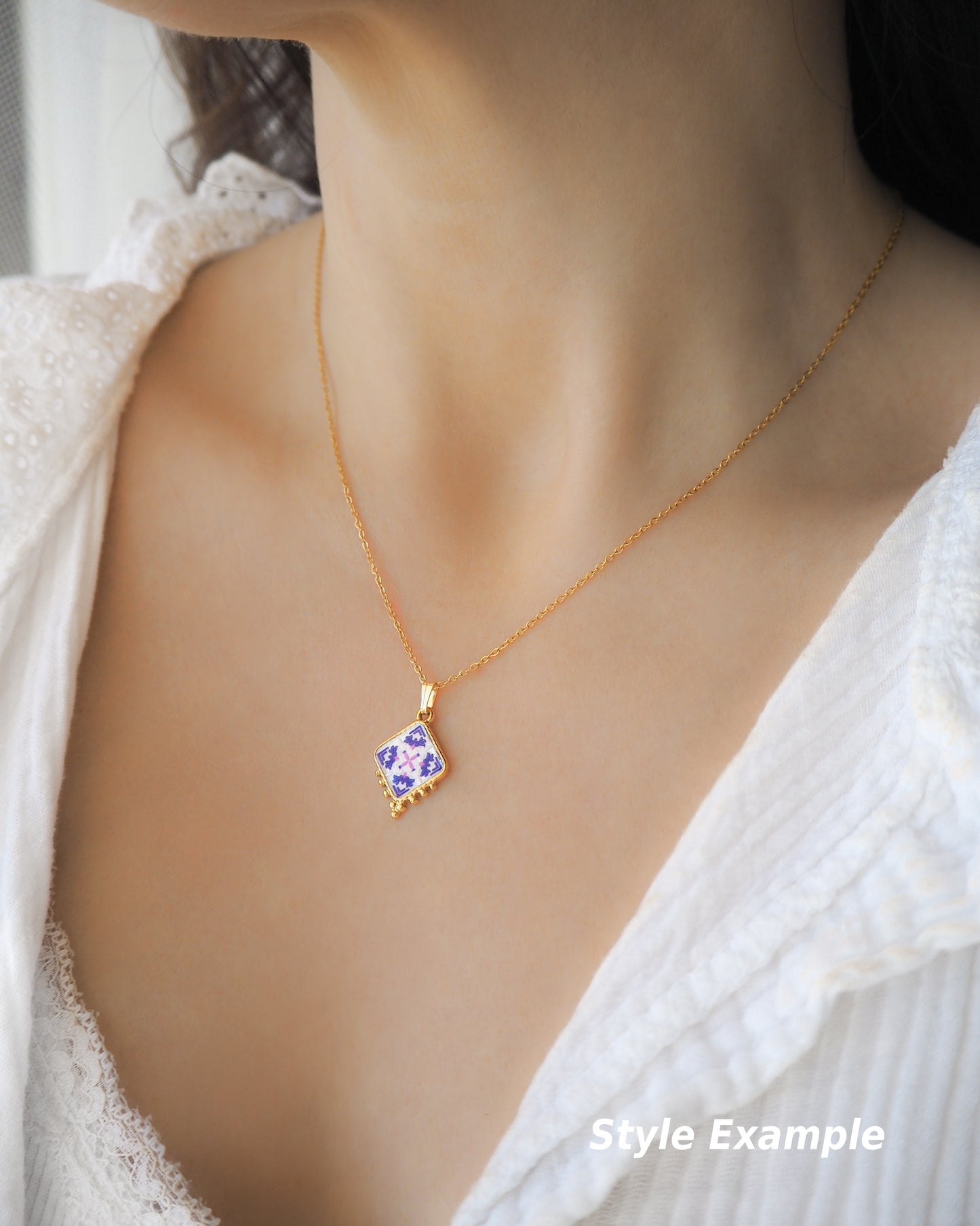 Model wearing a Gold Portuguese Tile Necklace on neck. Made with 18k gold stainless steel and white purple pink floral pendant inspired by the Portuguese Azulejo design pattern. Model is wearing a white blouse. 