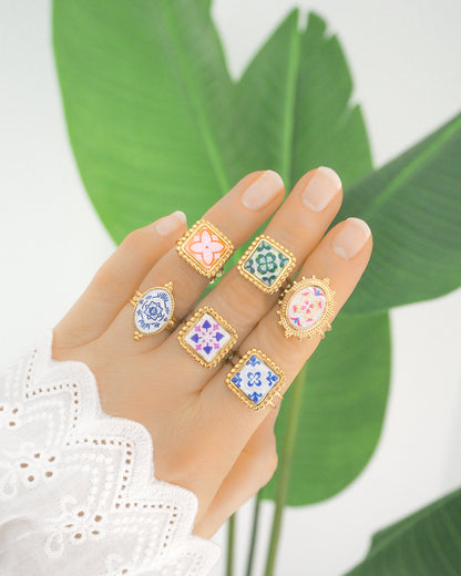 Hand wearing Gold Portuguese Tile Rings with green plant background. Rings are handmade with 18k gold stainless steel and are made with different patterns inspired by the Portuguese azulejos tiles. 
