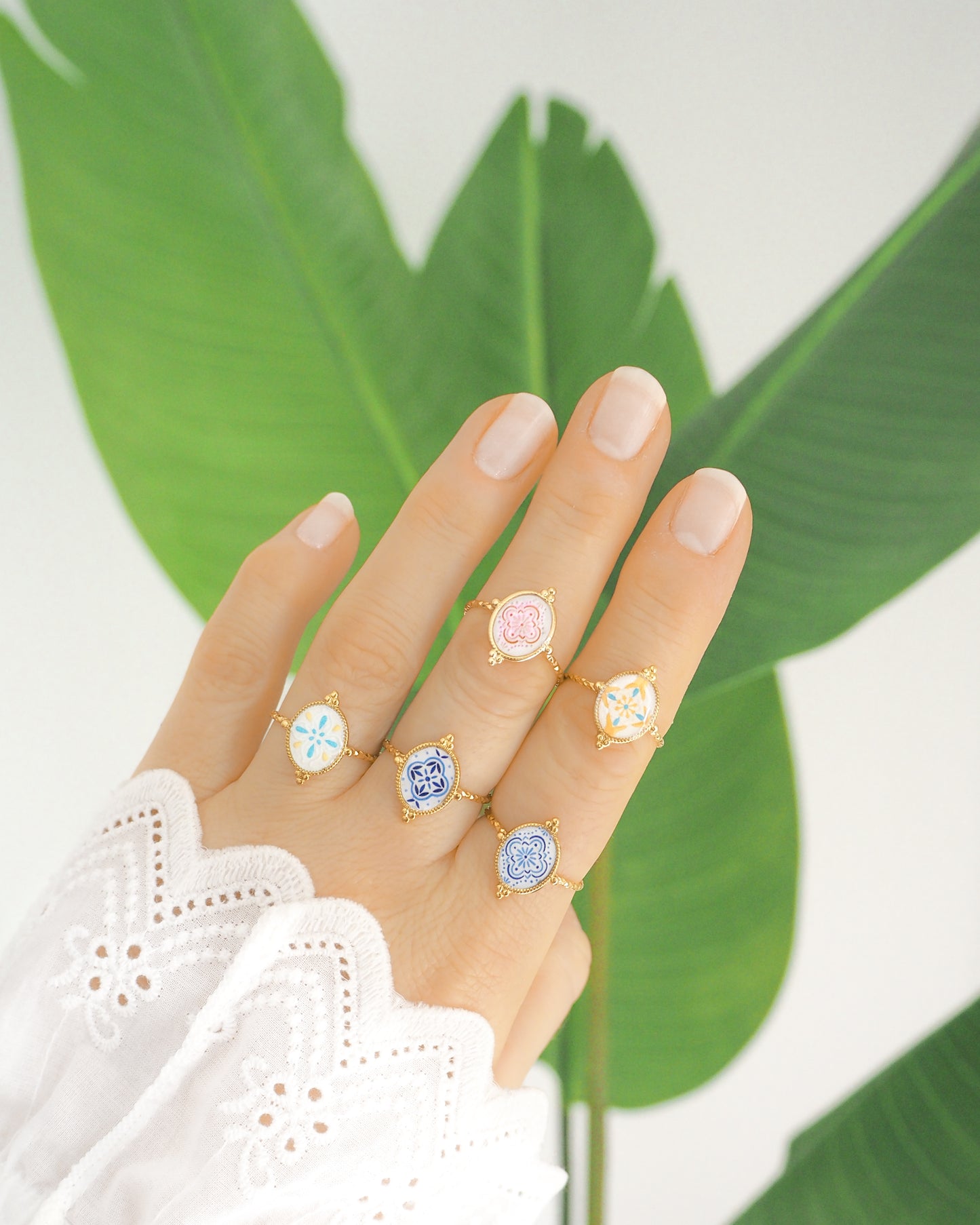 Hand wearing Gold Portuguese Tile Oval Rings with green plant background. Rings are handmade with 18k gold stainless steel and are made with different patterns inspired by the Portuguese azulejos tiles. 