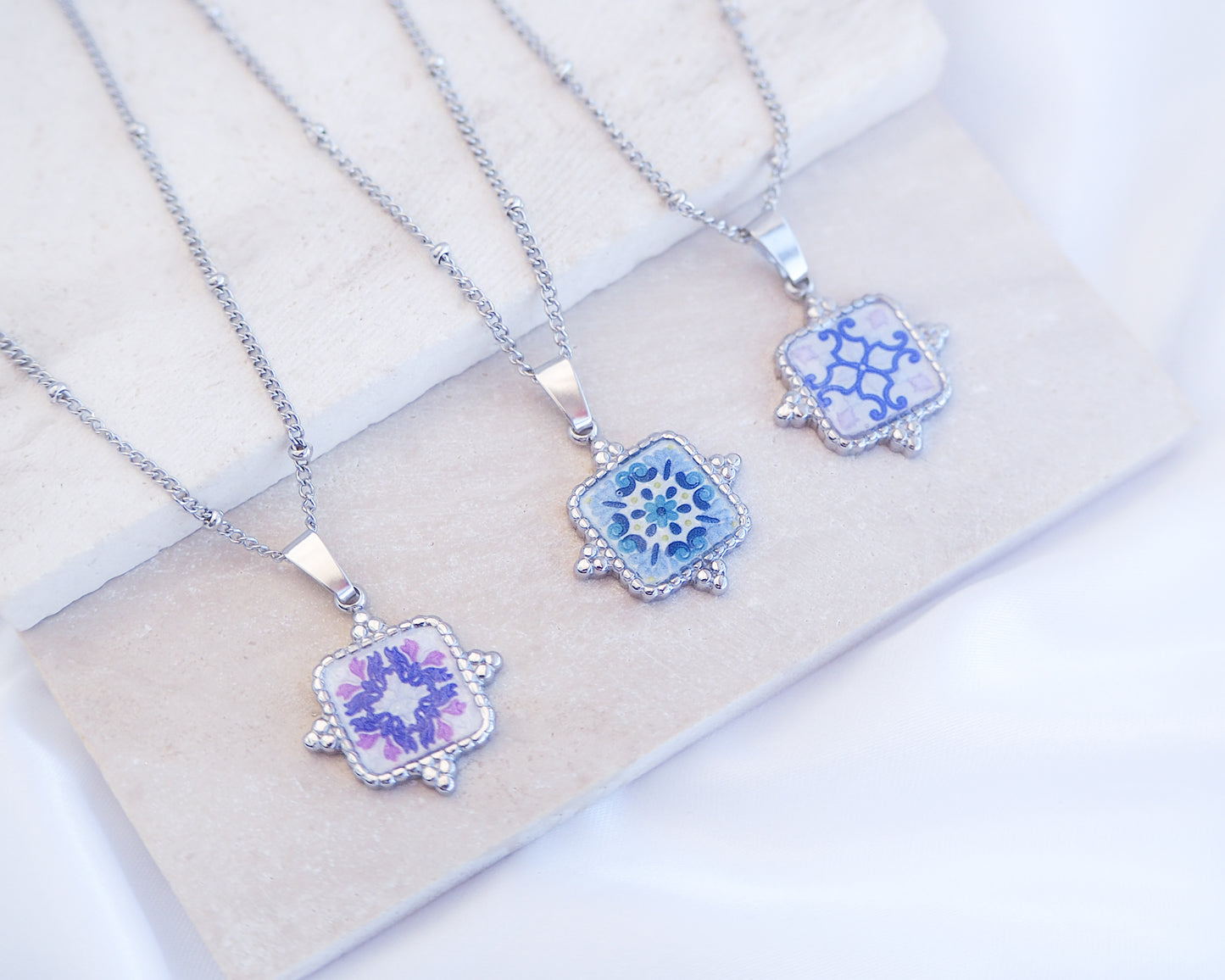 Stone display with close up of mix of Portuguese Tile Square Necklaces. Made with silver stainless steel. Showcasing white blue pattern pendant inspired by the Portuguese Azulejo design pattern. Perfect gift for Portugal lovers or as a Lisbon memory gift