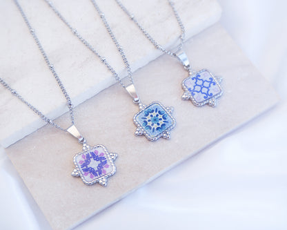 Stone display with close up of mix of Portuguese Tile Square Necklaces. Made with silver stainless steel. Showcasing white blue pattern pendant inspired by the Portuguese Azulejo design pattern. Perfect gift for Portugal lovers or as a Lisbon memory gift