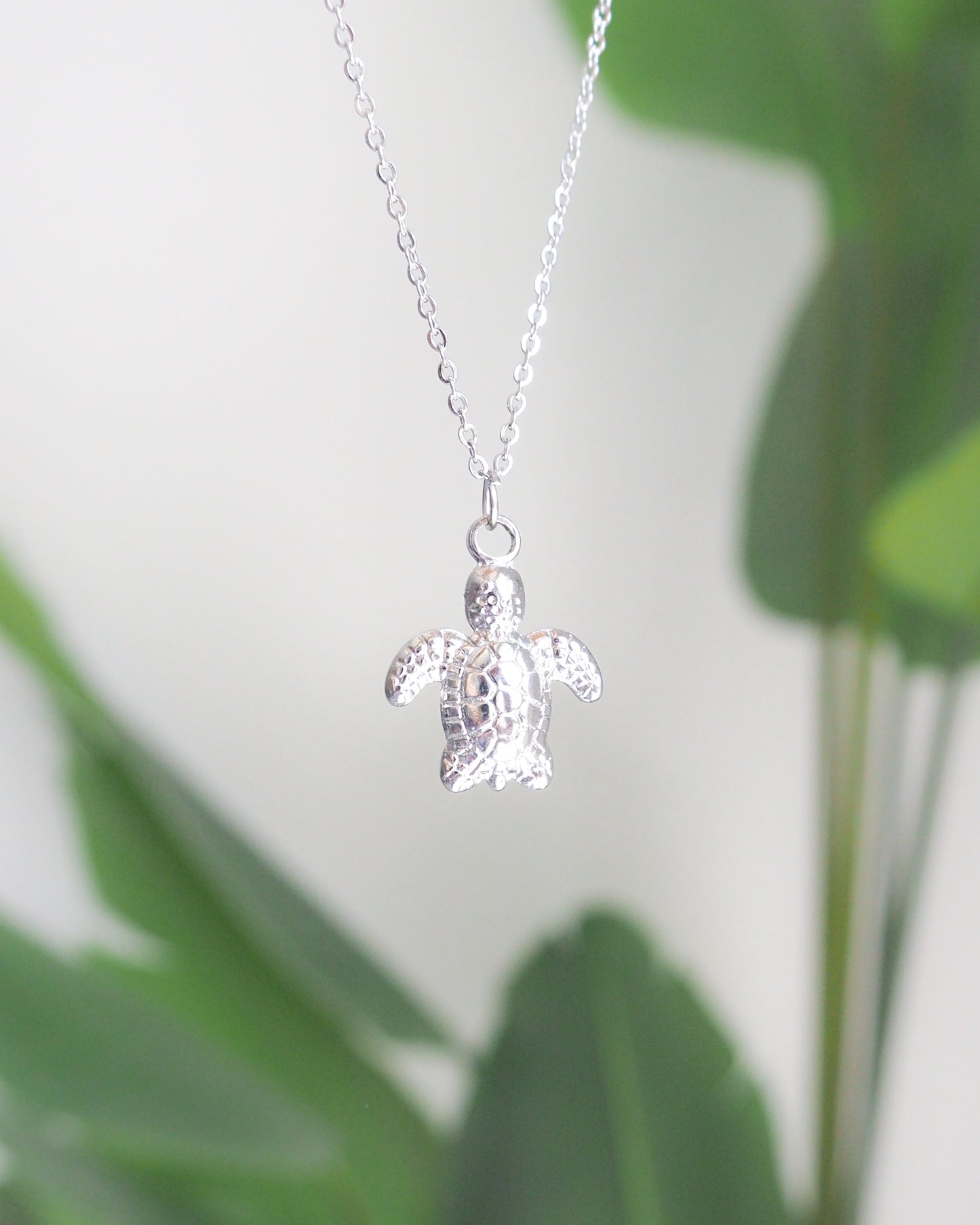 Silver turtle pendant necklace on a blurred green leaf background