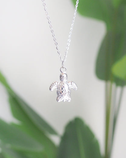 Silver turtle pendant necklace on a blurred green leaf background