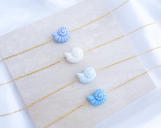 Blue Ceramic Seashell Nautilus Gold Necklaces all displayed on stone