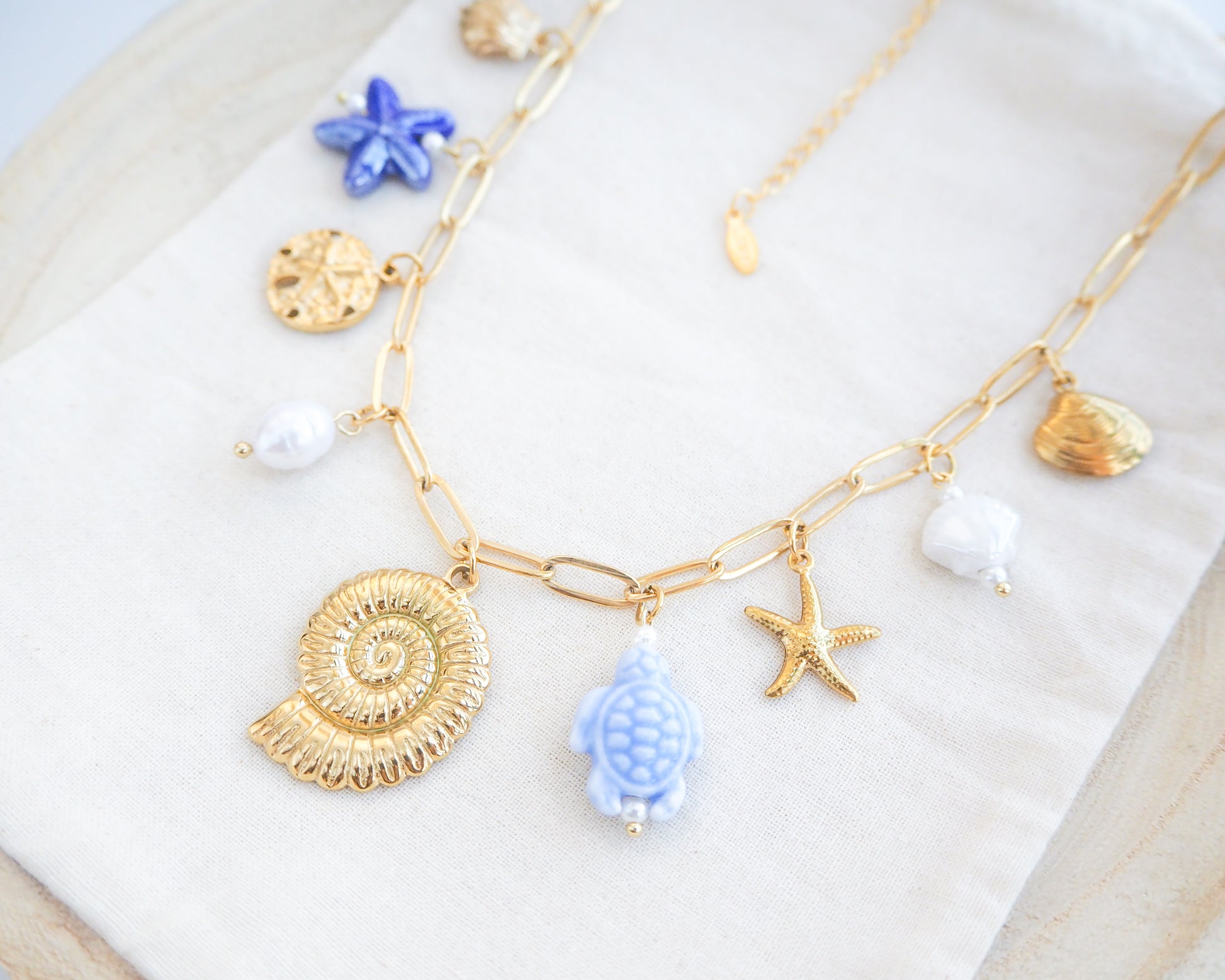 Side view Blue Ocean Ceramic Charm Necklace with 3 blue ceramic charms (turtle, starfish, shell), Shell pendant, sand dollar pendant, starfish pendant, 18k gold stainless steel chain on display 