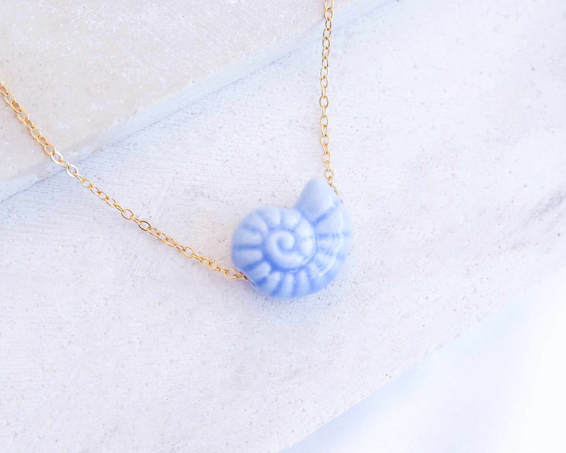 Blue Ceramic Seashell Nautilus Gold Necklace displayed on stone