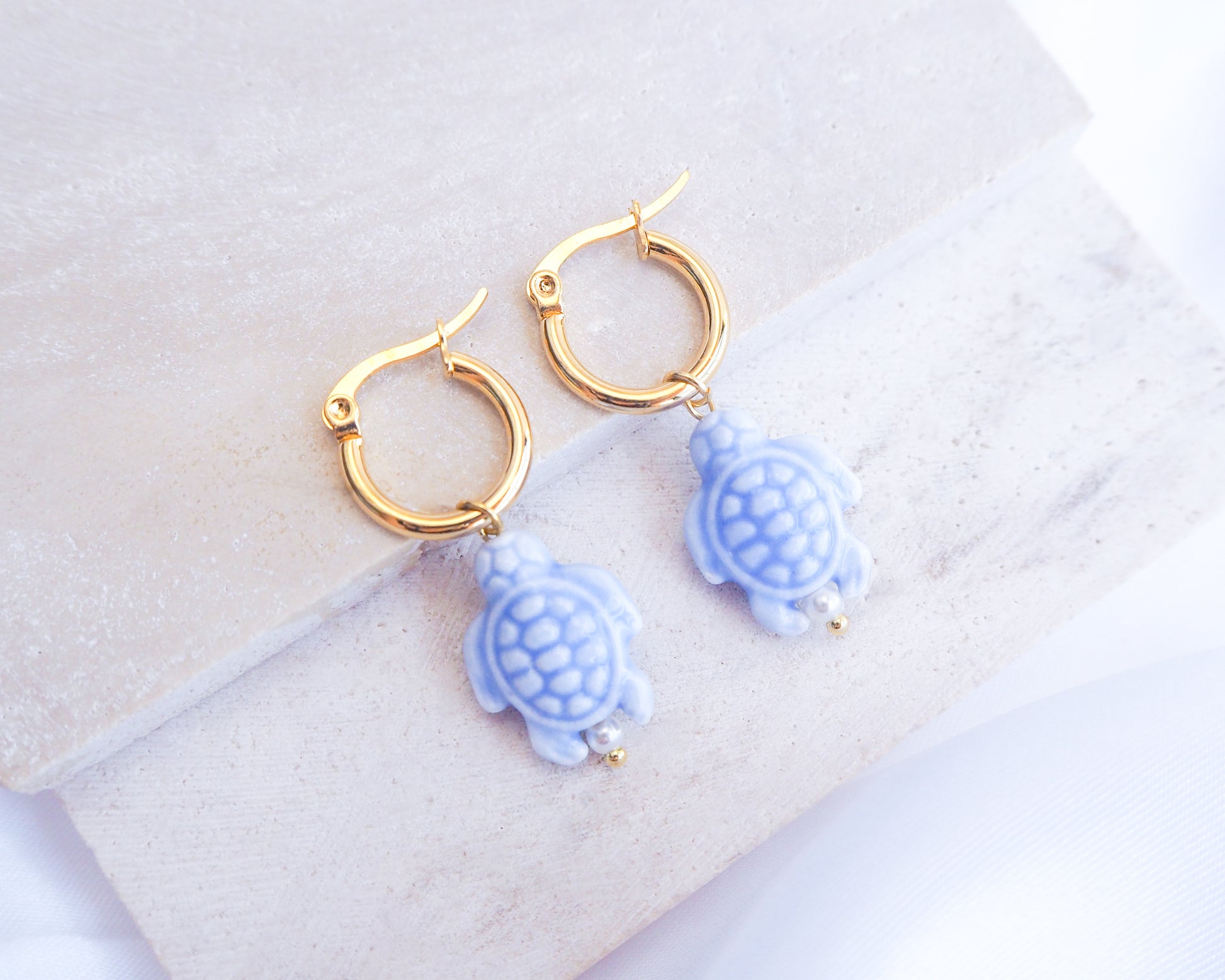 Gold hoop earrings with blue turtle charms on a white background
