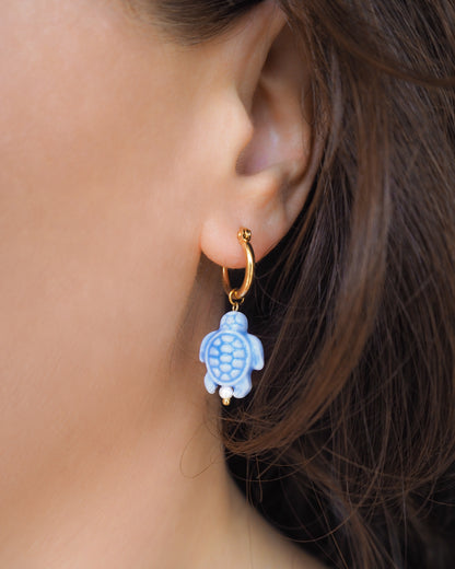 Close-up of an ear wearing a gold hoop earring with a blue turtle charm.