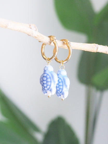 Gold hoop earrings with Blue Turtle ceramic beads on a branch with leaves in the background