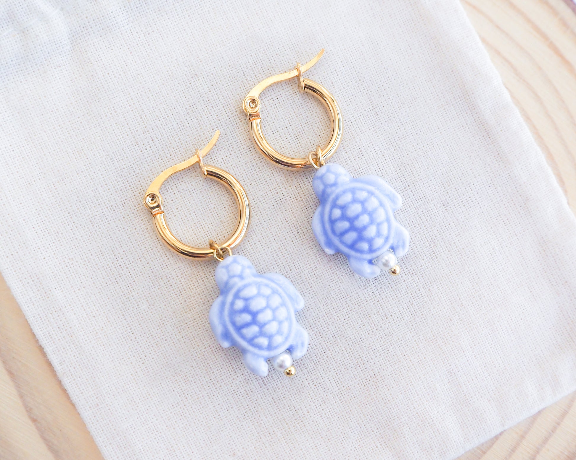 Pair of turtle-shaped earrings with gold hoops on a white fabric background