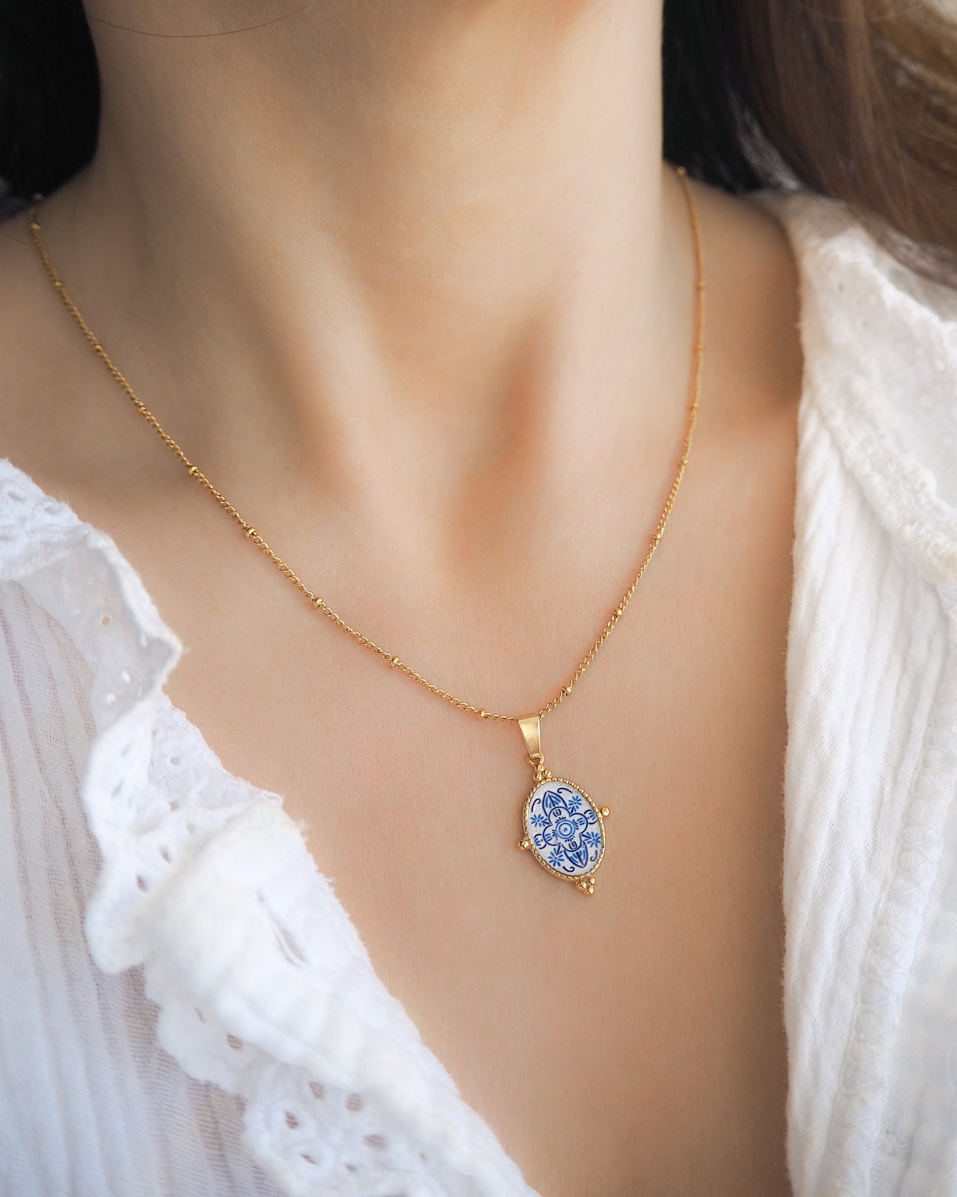 Model wearing Blue Portuguese Tile Oval Necklaces on neck. Made with 18k gold stainless steel and white blue mosaic pendant inspired by the Portuguese Azulejo design pattern. 
