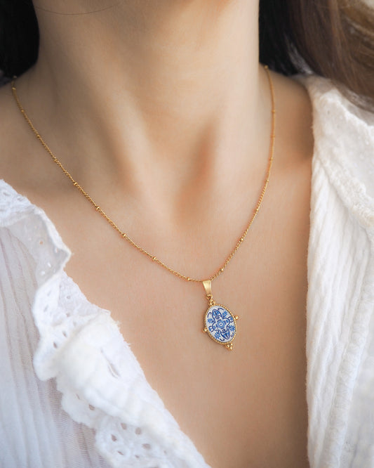 Model wearing Blue Portuguese Tile Oval Necklaces on neck. Made with 18k gold stainless steel and white blue mosaic pendant inspired by the Portuguese Azulejo design pattern. 