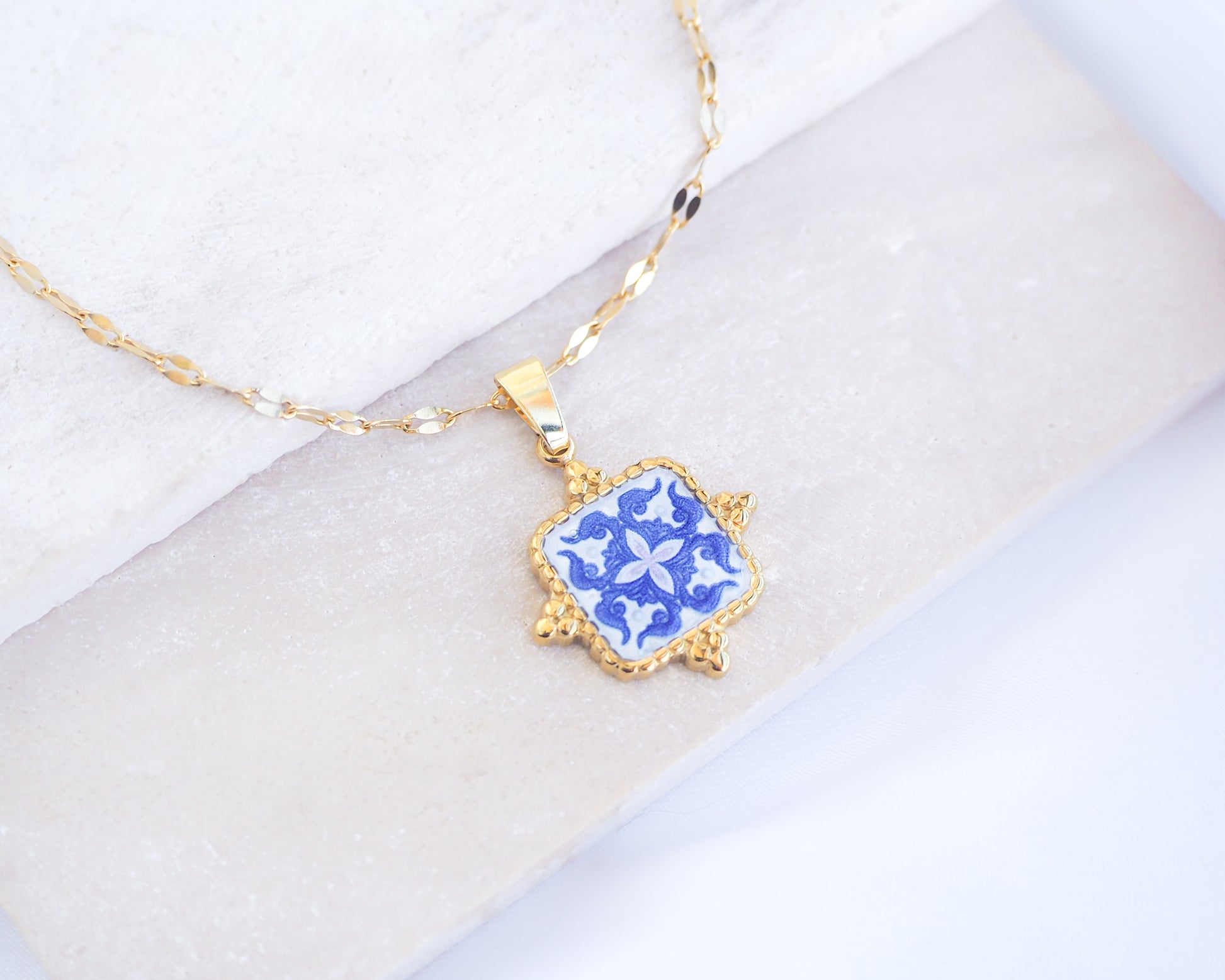 Close up of Blue Portuguese Tile Square Necklaces Blue on stone displayed. Made with 18k gold stainless steel and white blue mosaic pendant inspired by the Portuguese Azulejo design pattern. 