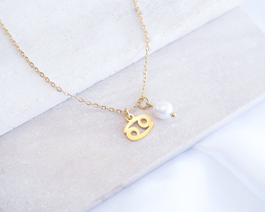 Gold Cancer Zodiac Pearl Necklace on stone displayed, made with 18k gold stainless steel and white freshwater pearl 