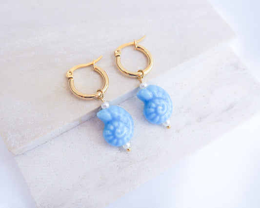 Gold ceramic seashell earrings with blue nautilus charms and gold hoop earrings on a white background
