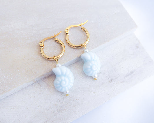 Gold hoop earrings with light blue seashell ceramic beads on a marble surface