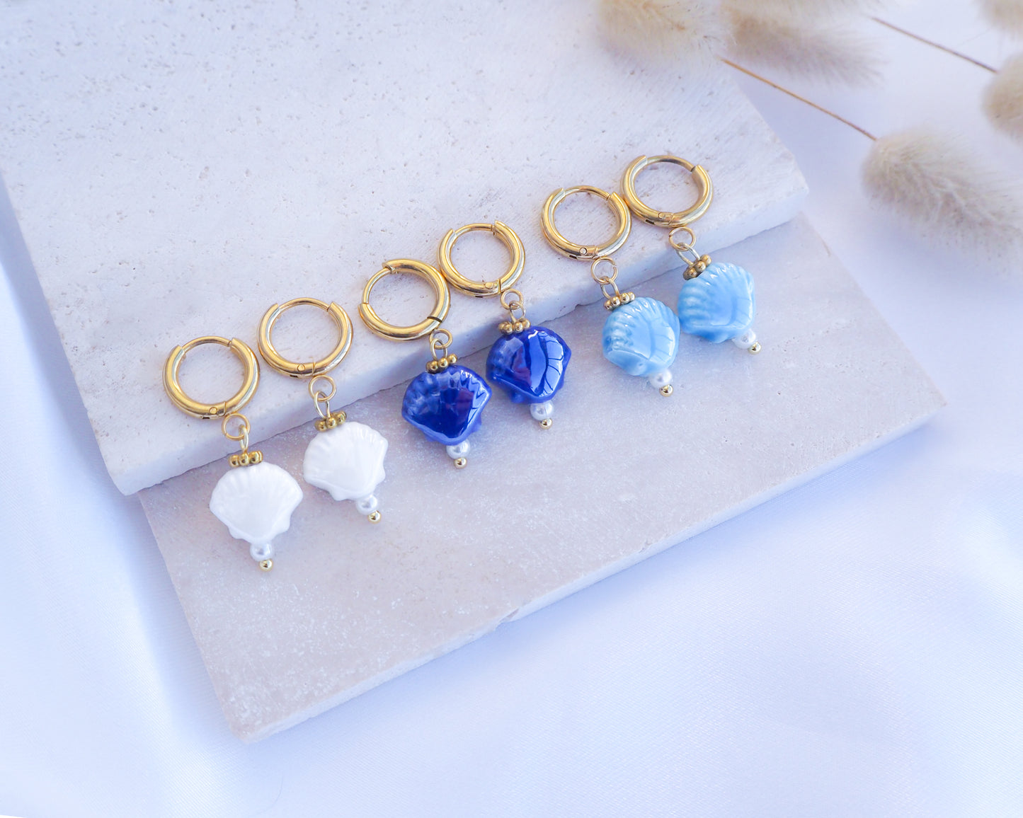 Ceramic Shell Gold Earrings with blue or white shell pendants on display