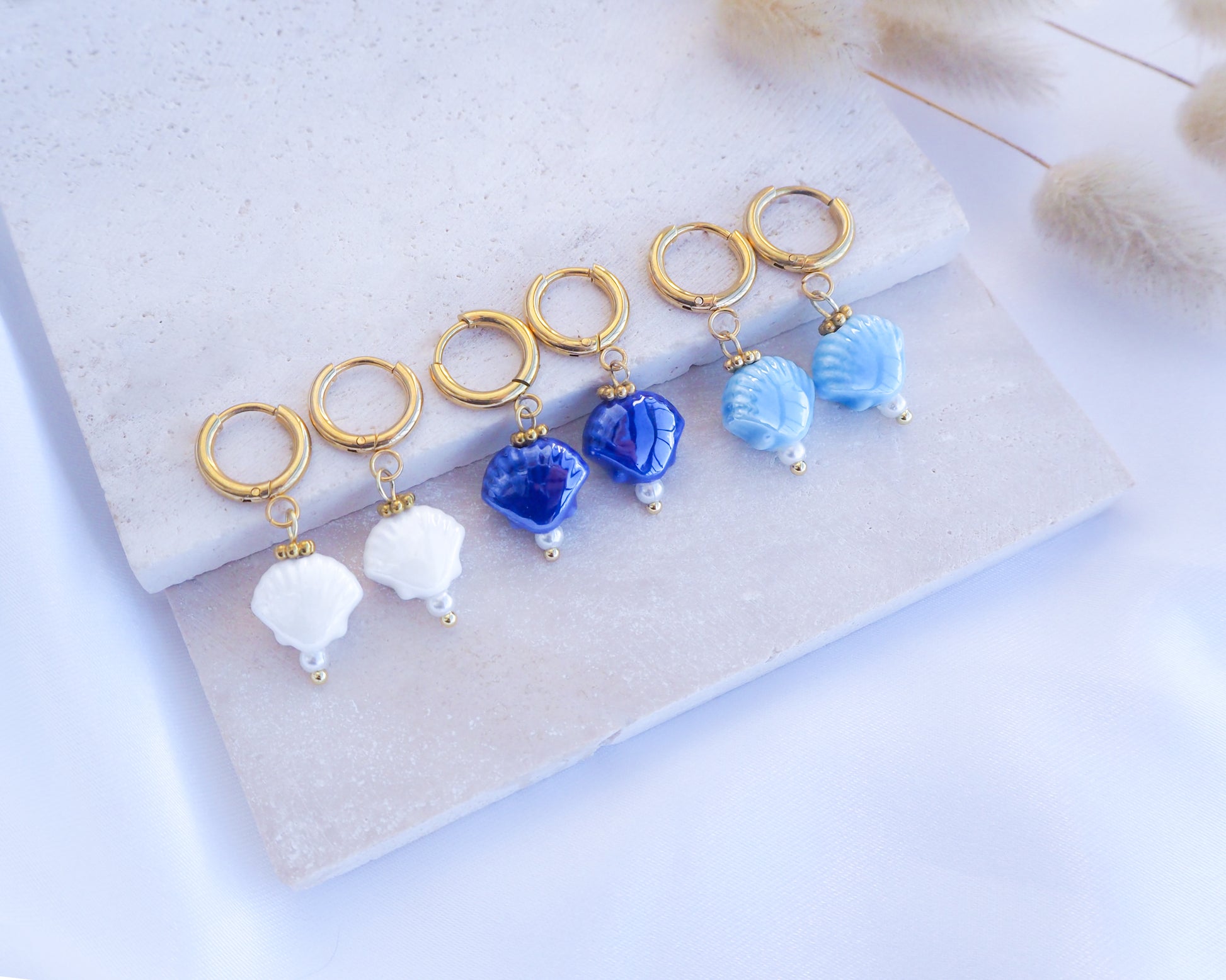 Ceramic Shell Gold Earrings with blue or white shell pendants on display