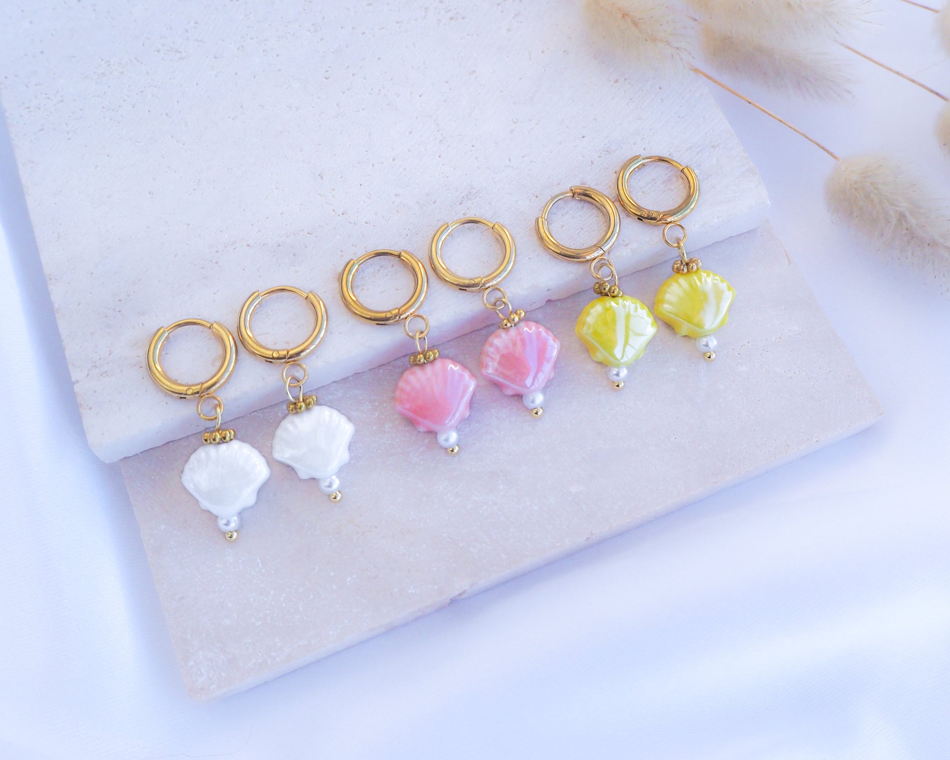 Ceramic Shell Gold Earrings with yellow, white or pink shell pendants on display