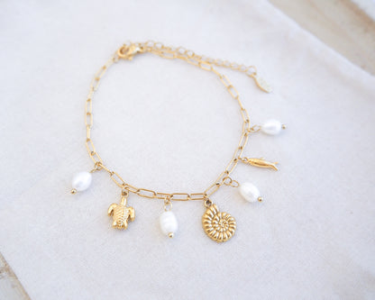 front view of Gold charm bracelet with freshwater pearls and ocean charms on display, tiny turtle pendant, tiny nautilus pendant, tiny sardine fish pendant bracelet. 