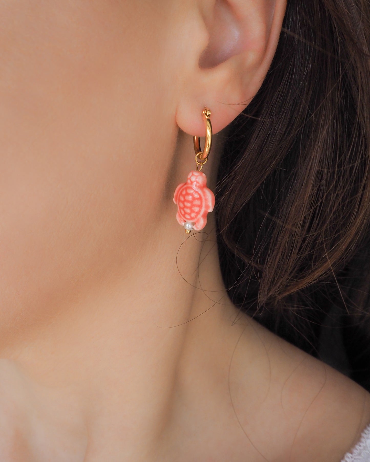 Close-up of a person wearing a coral pink turtle ceramic earring with a gold hoop.