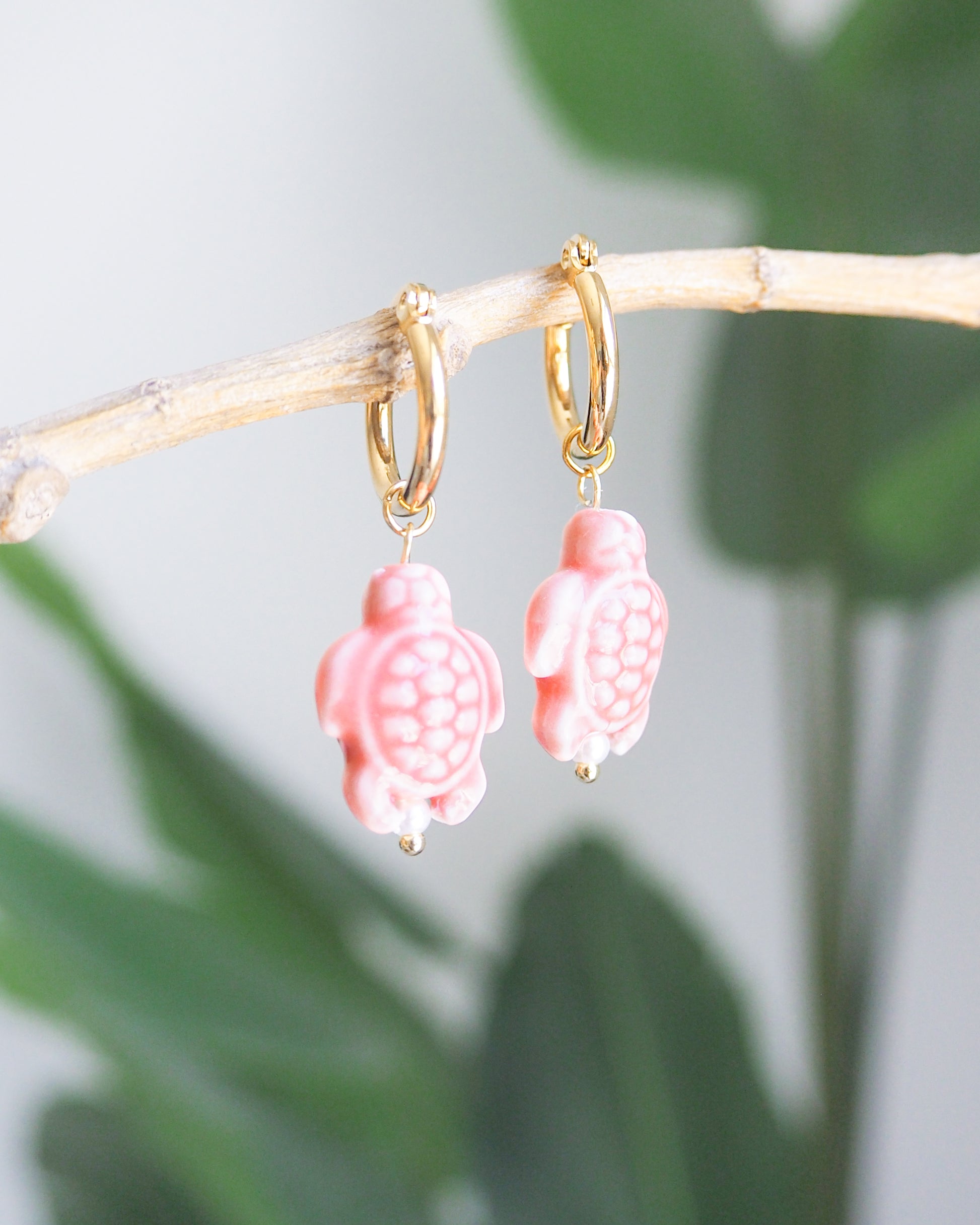 coral pink turtle ceramic earrings on gold hoops with a natural background