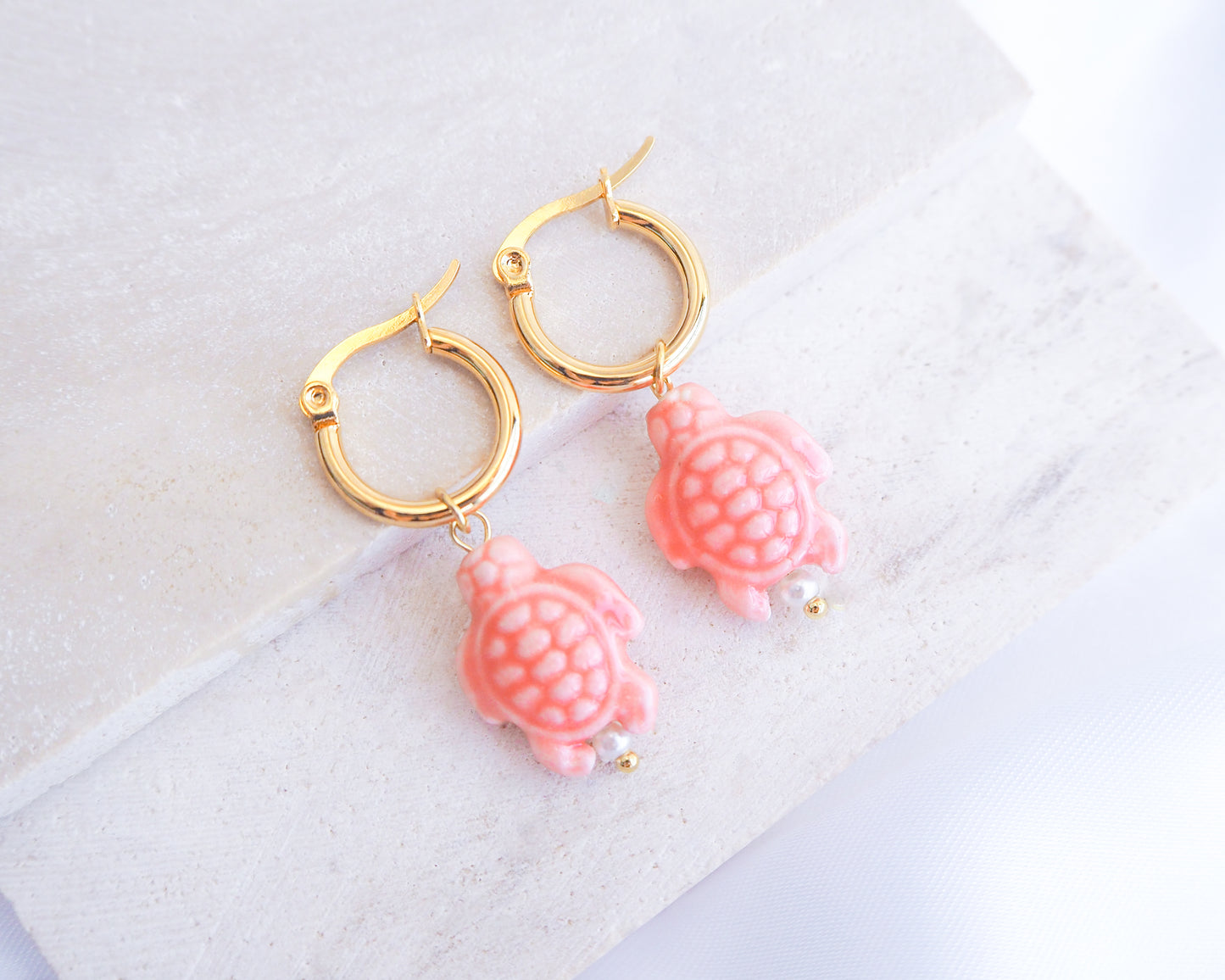 Gold hoop earrings with Coral Pink Turtle charms on a light background