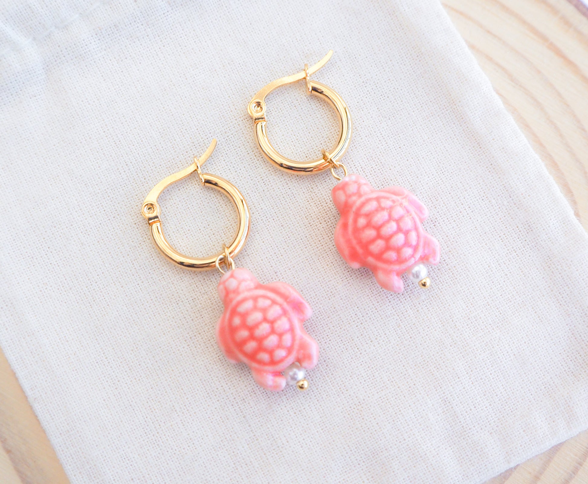 Gold hoop earrings with pink turtle ceramic charms on a white surface