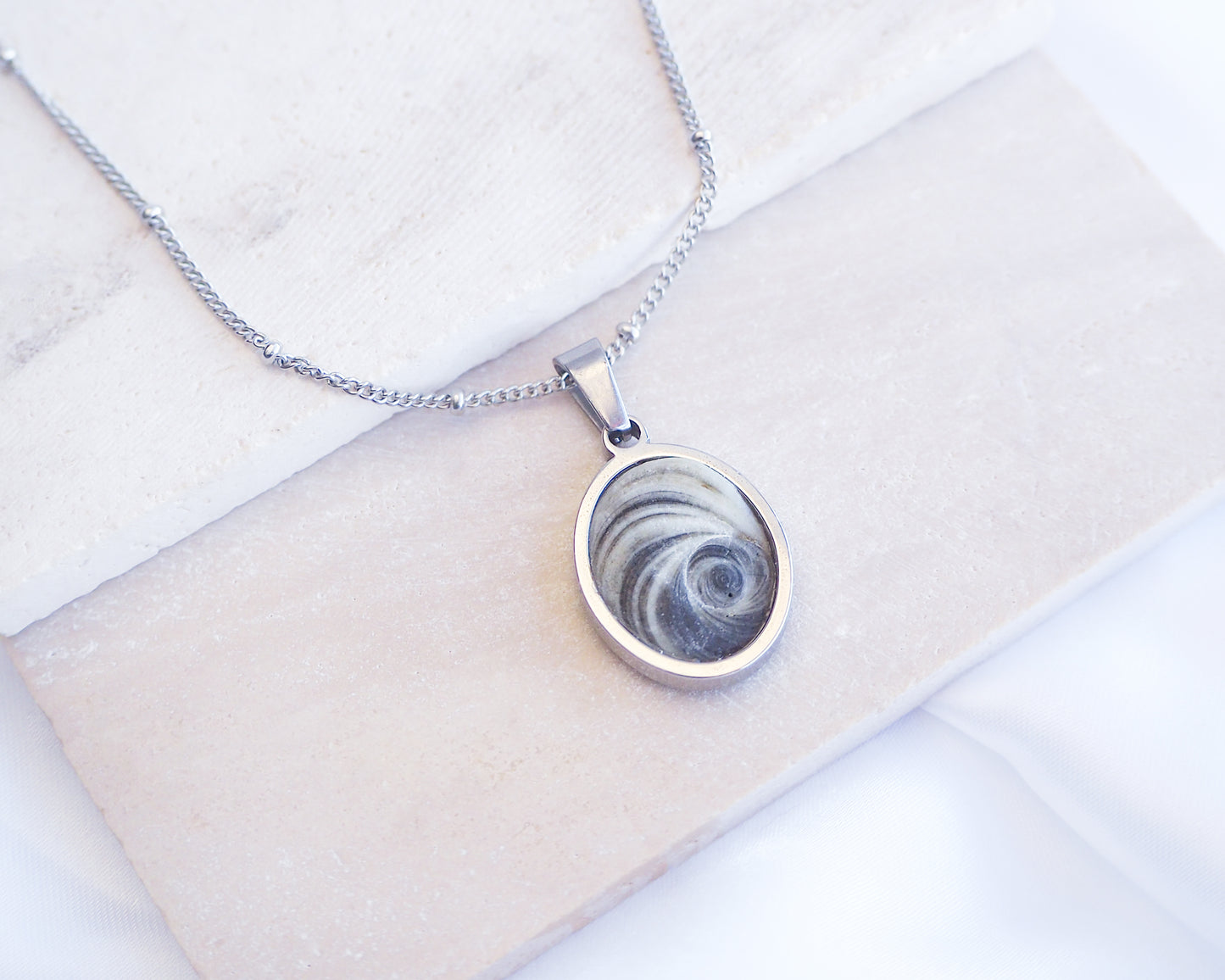Dark Grey Eye of Saint Lucia Silver Necklace front view displayed on stone, silver stainless steel shiva eye pendant necklace, Saint Lucy Eye, operculum pendant