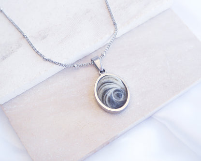 Dark Grey Eye of Saint Lucia Silver Necklace front view displayed on stone, silver stainless steel shiva eye pendant necklace, Saint Lucy Eye, operculum pendant