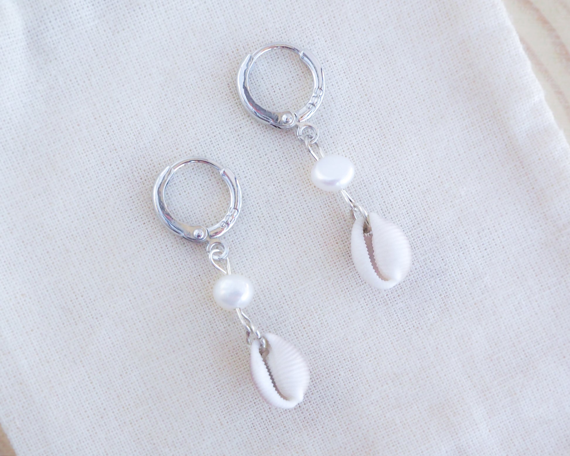 Close up of cowrie shell earrings with freshwater pearls and 925 silver earrings on cotton displayed, coastal wedding jewelry