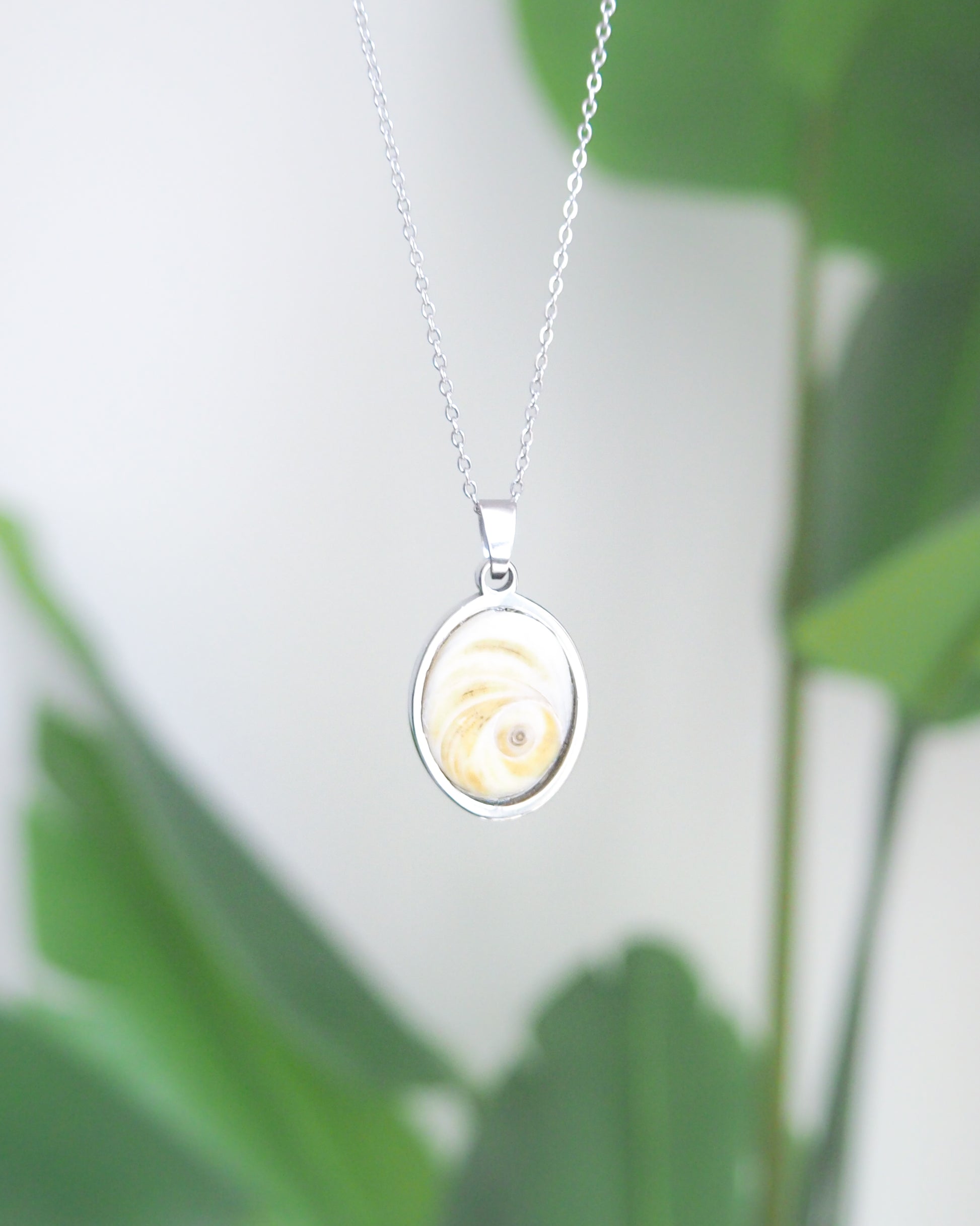 Eye of Saint Lucia Silver Necklace front view with plant background, silver stainless steel shiva eye pendant necklace, Saint Lucy Eye, operculum pendant