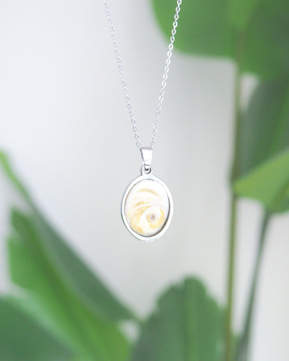 Eye of Saint Lucia Silver Necklace front view with plant background, silver stainless steel shiva eye pendant necklace, Saint Lucy Eye, operculum pendant