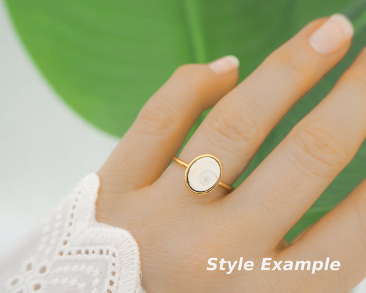 Hand of model with finger with gold bezel ring with a ivory shiva eye. White Eye of Saint Lucia Gold Ring on stone displayed, 18k gold stainless steel shiva eye operculum, Saint Lucy Eye, operculum pendant