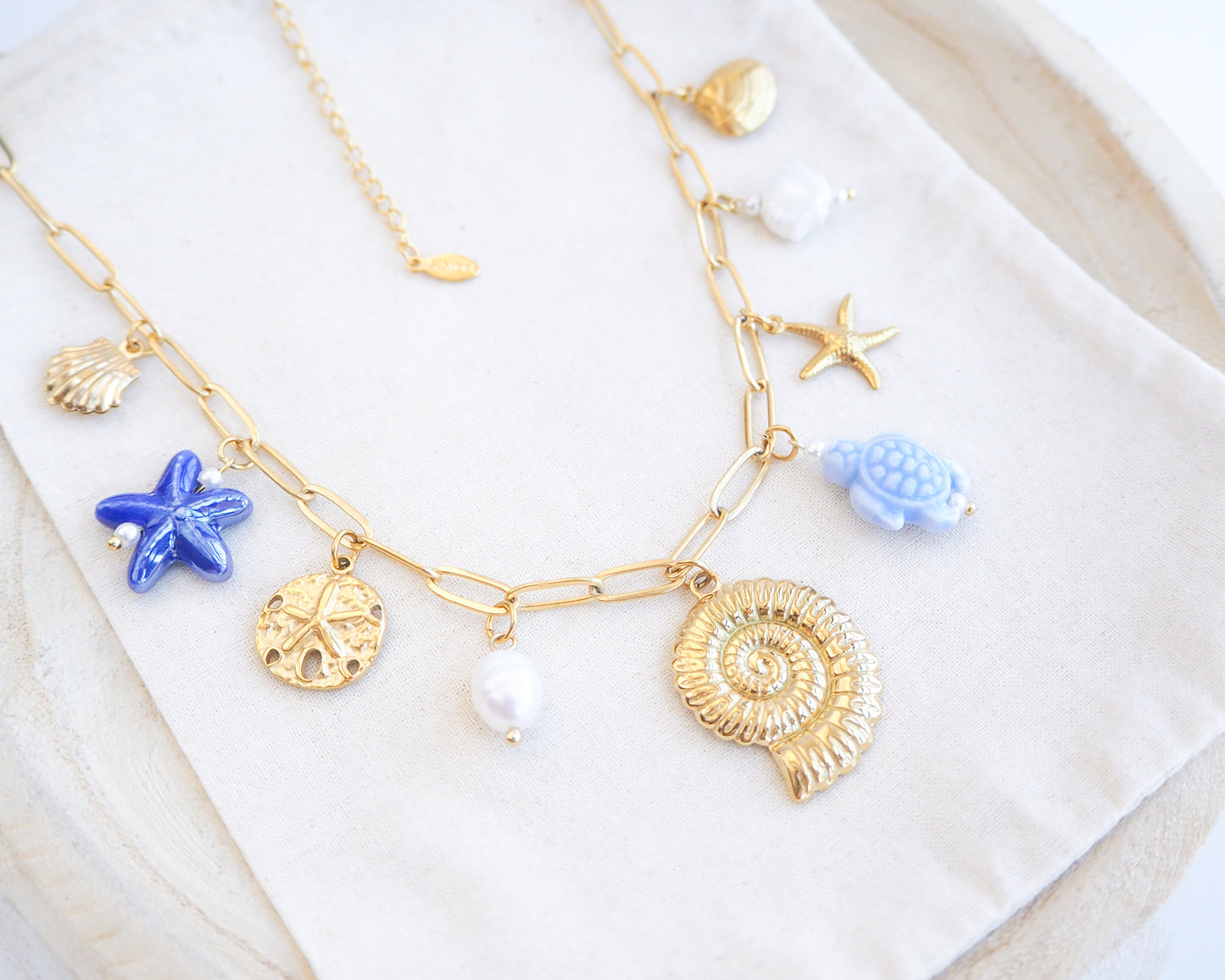 Close up of Blue Ocean Ceramic Charm Necklace with 3 blue ceramic charms (turtle, starfish, shell), Shell pendant, sand dollar pendant, starfish pendant, 18k gold stainless steel chain on display 