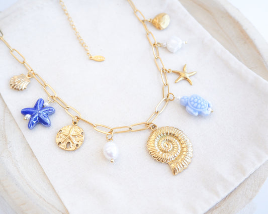 Close up of Blue Ocean Ceramic Charm Necklace with 3 blue ceramic charms (turtle, starfish, shell), Shell pendant, sand dollar pendant, starfish pendant, 18k gold stainless steel chain on display 
