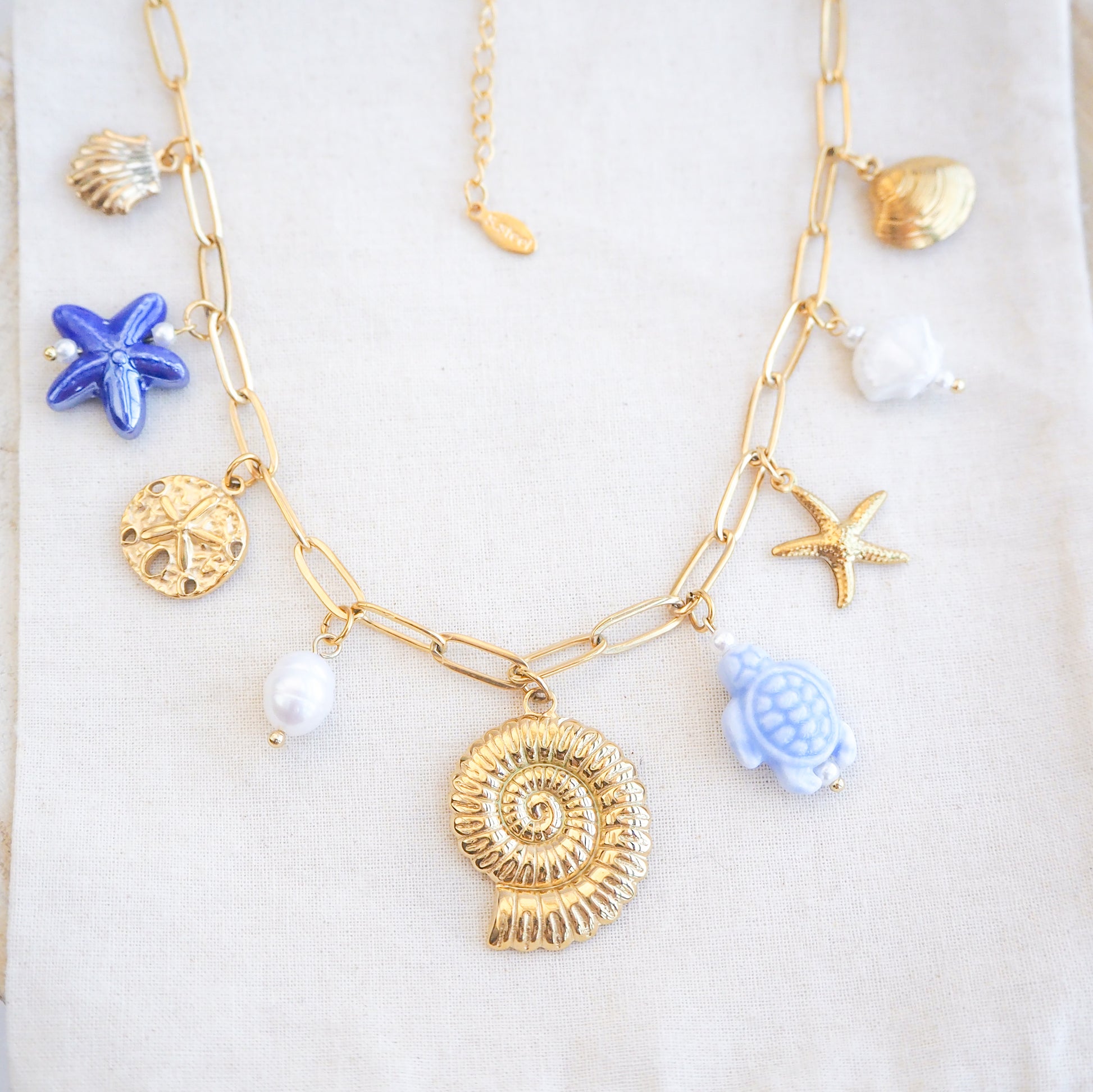 Front view of Blue Ocean Ceramic Charm Necklace with 3 blue ceramic charms (turtle, starfish, shell), Shell pendant, sand dollar pendant, starfish pendant, 18k gold stainless steel chain  