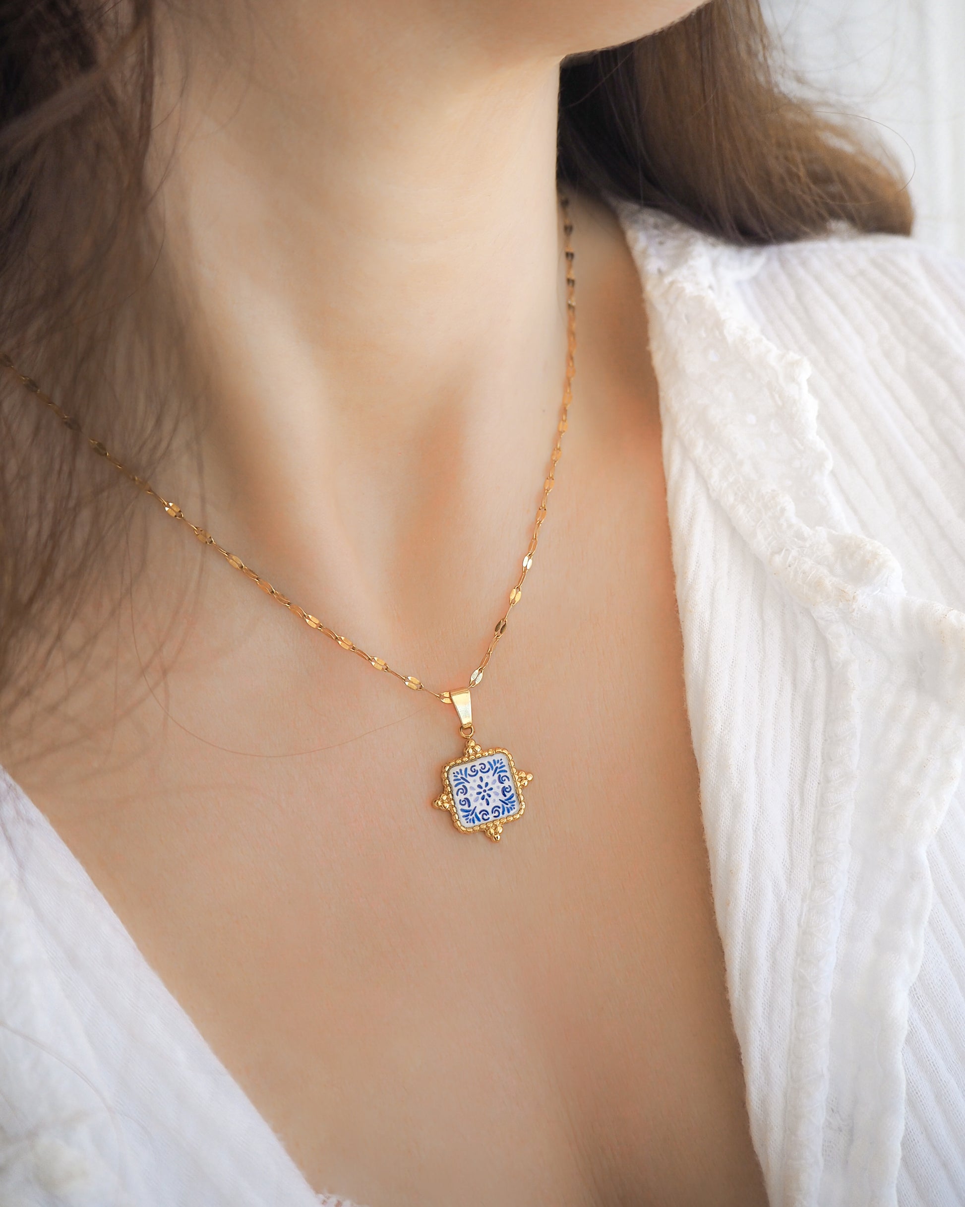 Model wearing Blue Portuguese Tile Square Necklaces Gold on neck. Made with 18k gold stainless steel and white blue mosaic pendant inspired by the Portuguese Azulejo design pattern. 