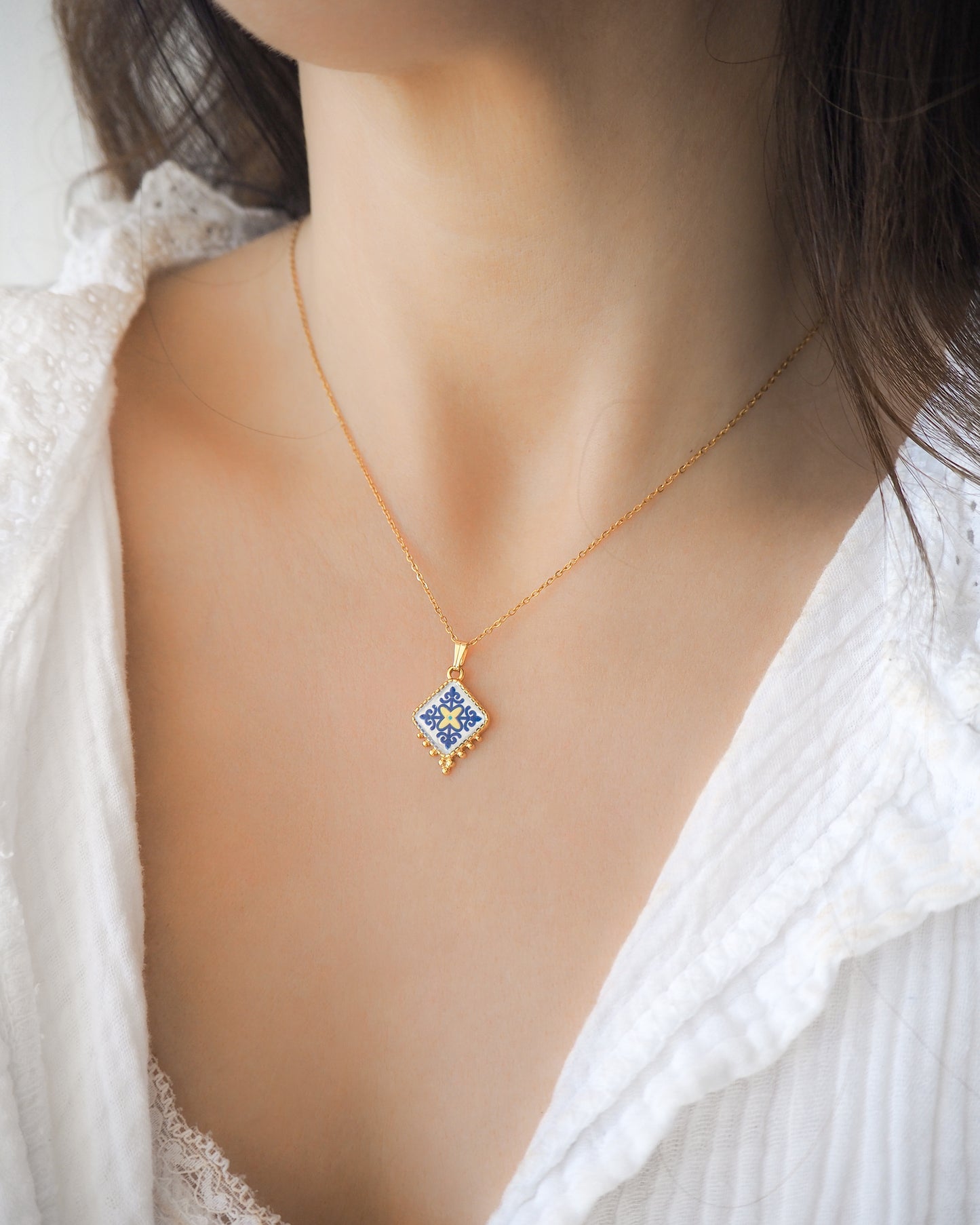 Model wearing Blue Yellow Portuguese Tile Necklace Gold on stone displayed. Made with 18k gold stainless steel and blue yellow pendant inspired by the Portuguese Azulejo design pattern. 