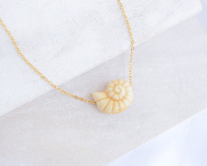 Gold Bege Ceramic Seashell Nautilus Necklace displayed on stone