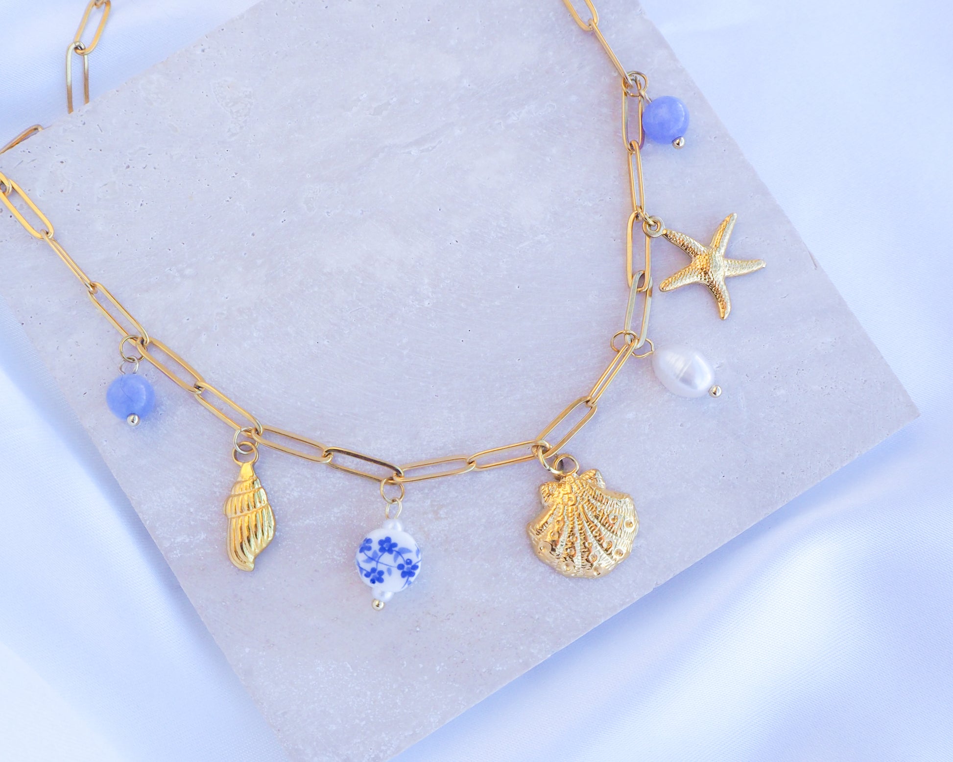 Oceanic Charm Necklace with Shells and Starfish Pendants, Freshwater Pearls and Gemstones on stone