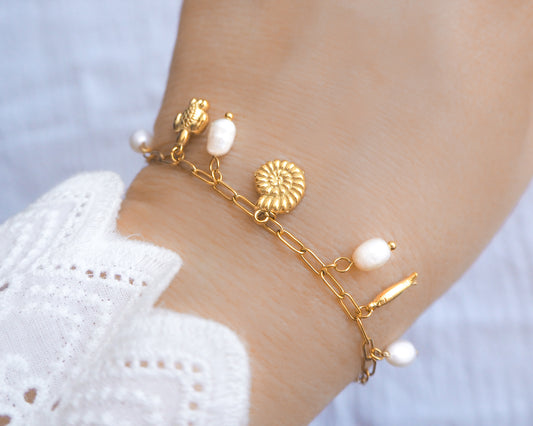 Gold charm bracelet with freshwater pearls and ocean charms on wrist model, tiny turtle pendant, tiny nautilus pendant, tiny sardine fish pendant bracelet. 
