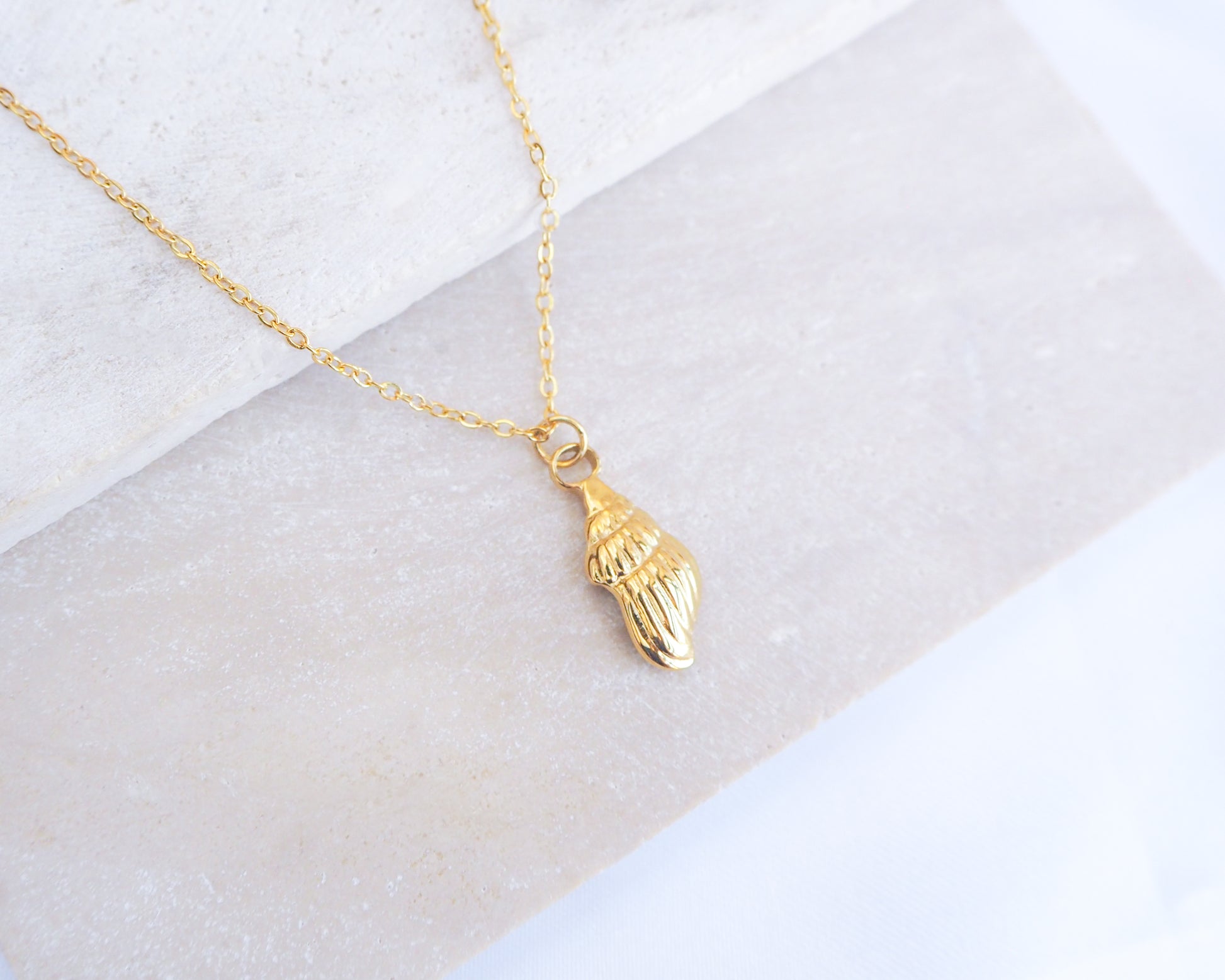 Gold Conch shell pendant necklace on a white marble surface
