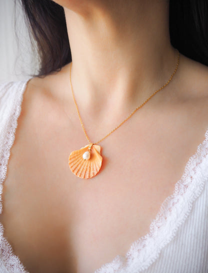 Model wearing Coral Orange Scallop Shell Pearl Gold Necklace II on stone displayed, Pilgrims Scallop Shell from Portugal with freshwater pearl and gold chain. 