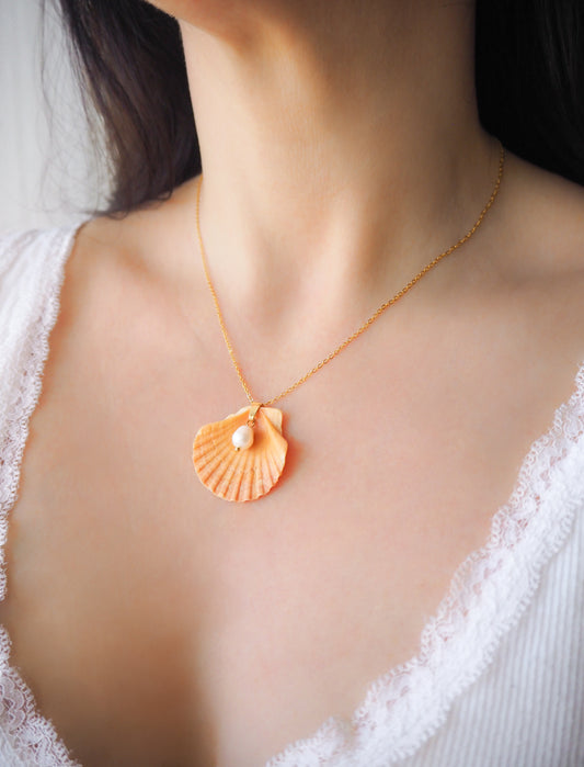 Model wearing Coral Orange Scallop Shell Pearl Gold Necklace II on stone displayed, Pilgrims Scallop Shell from Portugal with freshwater pearl and gold chain. 