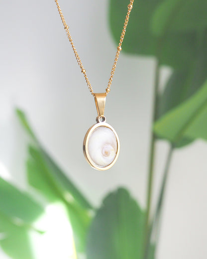 Front view Ivory White Eye of Saint Lucia Gold Necklace with green plant background, 18k gold stainless steel shiva eye pendant necklace, Saint Lucy Eye, operculum pendant
