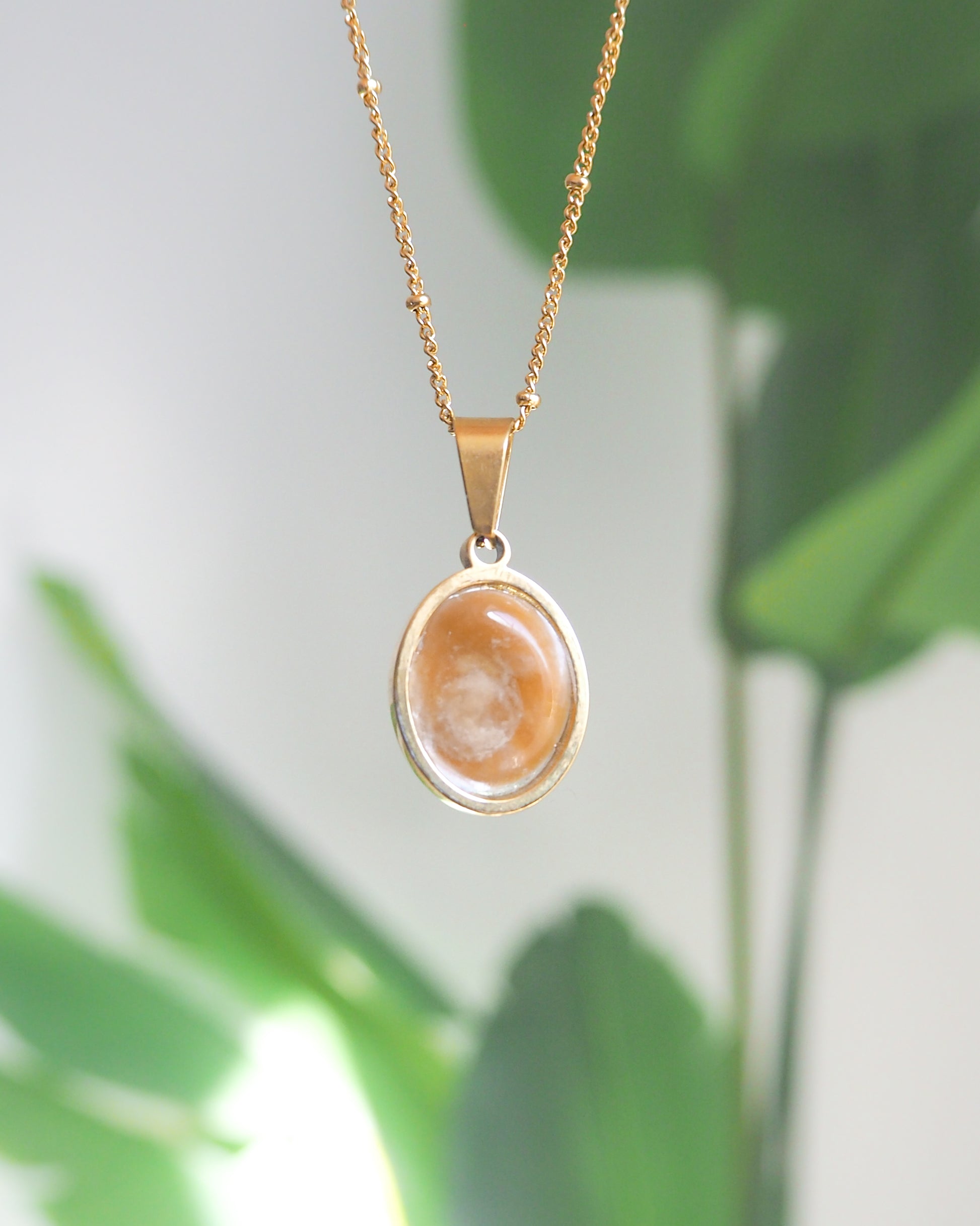 Back of Ivory White Eye of Saint Lucia Gold Necklace with green plant background, 18k gold stainless steel shiva eye pendant necklace, Saint Lucy Eye, operculum pendant